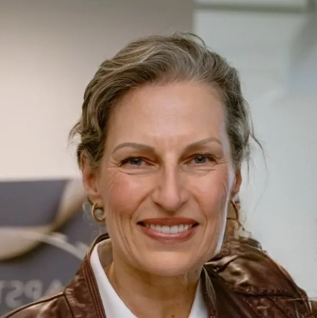 Kirsten Swenson A woman with grey hair and wearing a brown jacket.